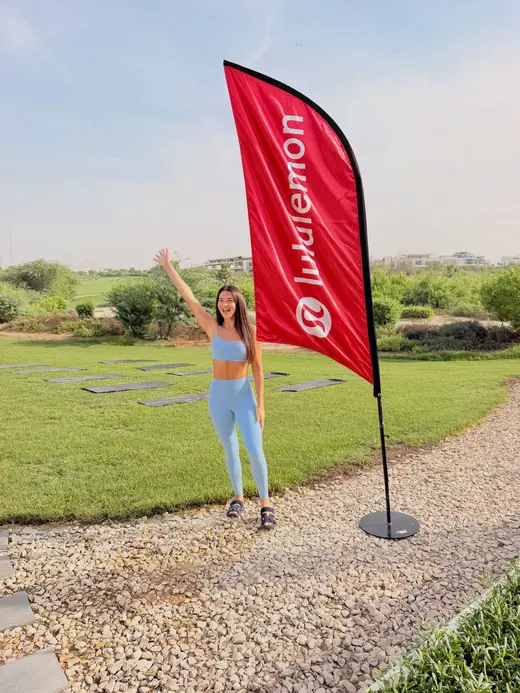 Renaé waving beside a lululemon flag on a green lawn